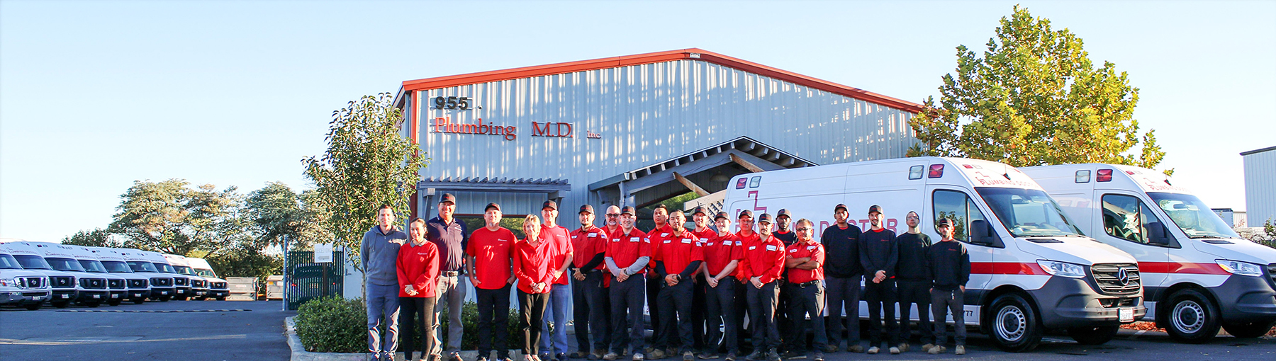 Group photo of Plumbing Doctor team standing next to ambulance style vehicles with the Plumbing Doctor building in the background.