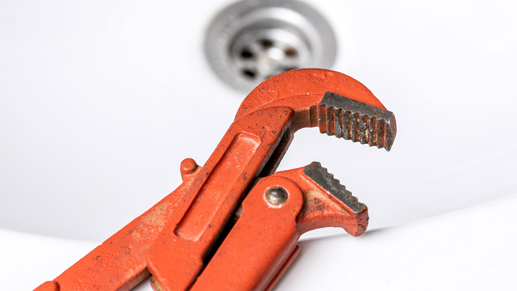Close-up view of orange pipe wrench leaning against a white sink.